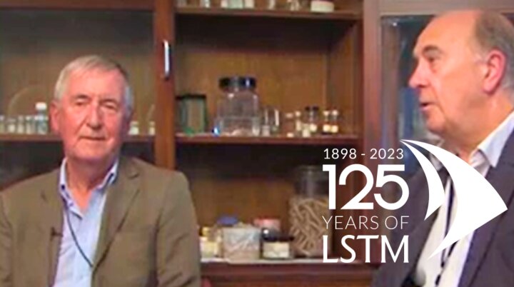 Professors Geoff Gill and Nick Beeching being interviewed in the laboratory in front of a display cabinet of historical laboratory equipment and samples 